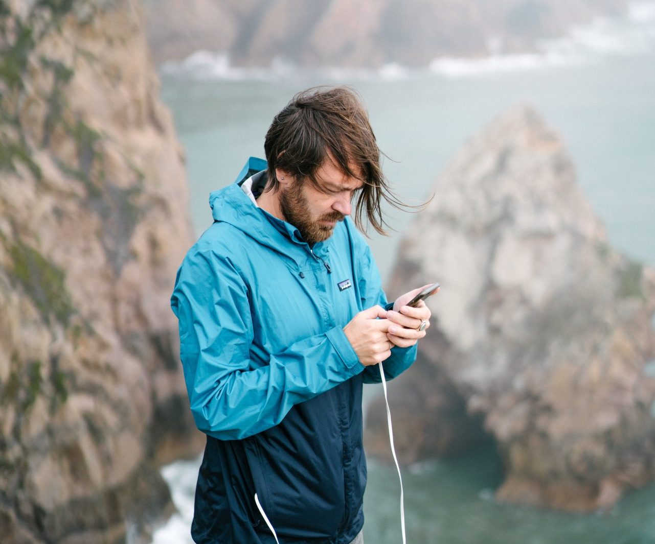 focused-man-with-smartphone-on-cliff-4330271